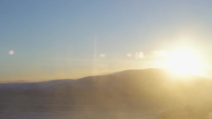 Sun peaks over mountain top shining over snow covered boulders and ground