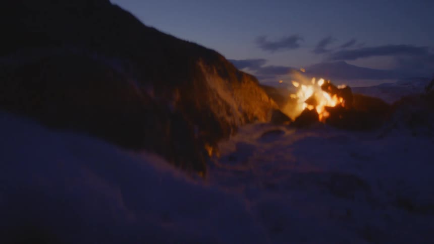 Campfire burning over the snow in the mountains at sunset