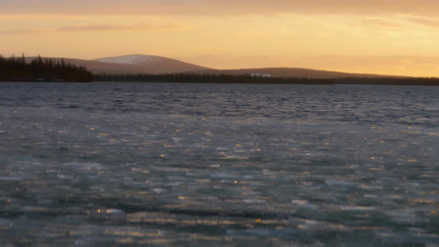 Frozen water on the surface of a lake near the mountains at sunset
