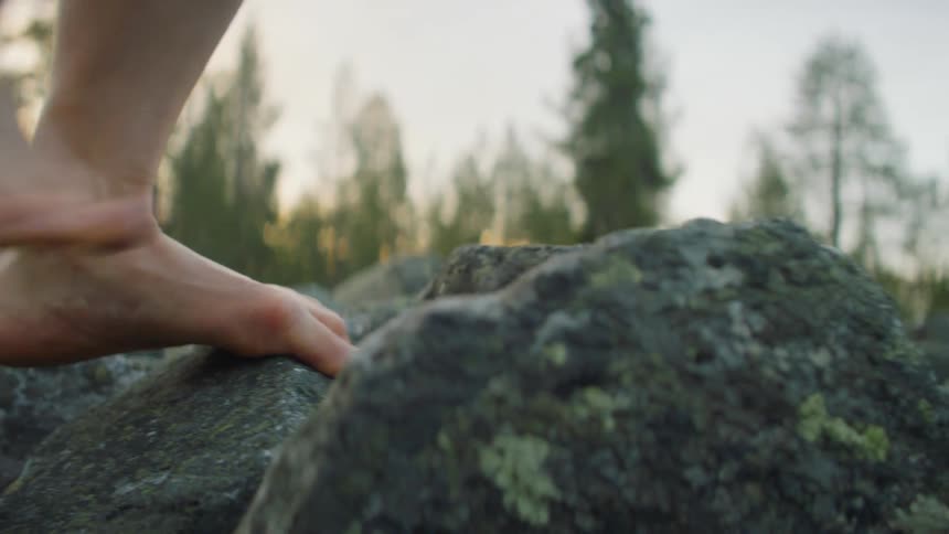A man walks barefoot over large rocks in a forest