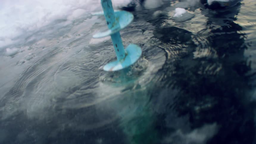 A person using a drill to drill a hole in ice water and snow