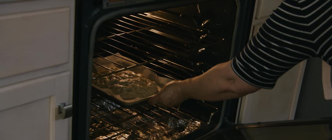 Woman wearing red pinstripe apron places dough into oven