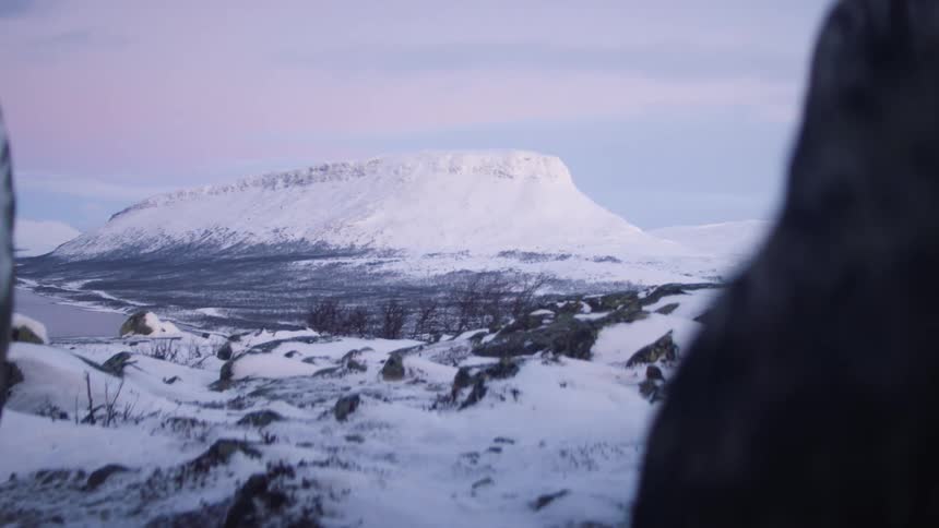 A flat topped mountain covered in snow in a snowy countryside during the day