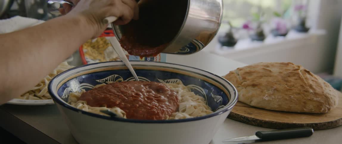 Cook adds sauce to pasta in big bowl