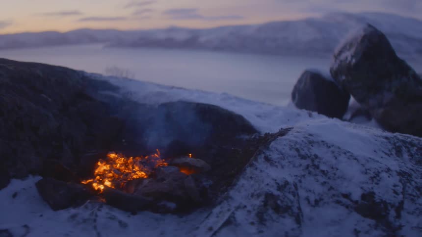 Smoldering embers in a campfire over the snow near the mountains at sunset