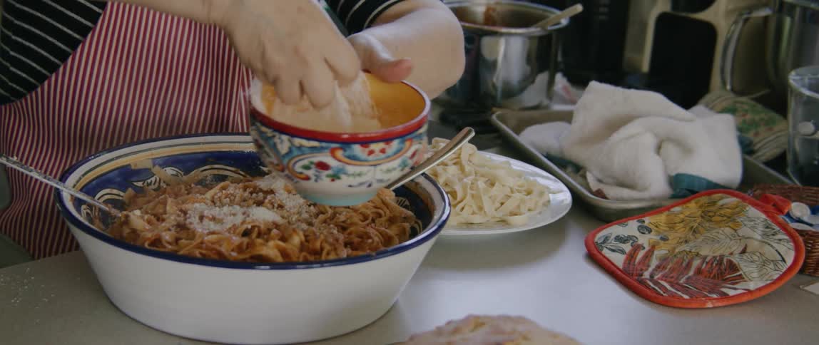 A woman in the kitchen adding cheese to a bowl of spaghetti