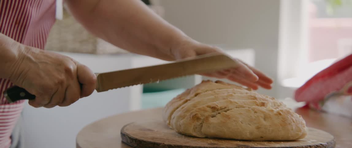 An elderly woman in a striped apron cutting a loaf of homemade bread
