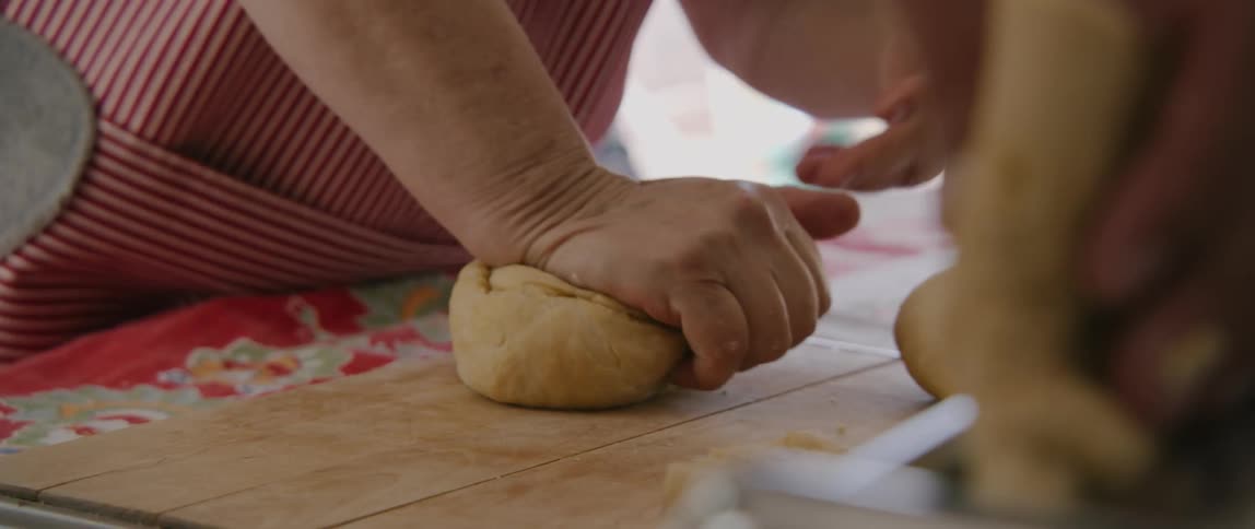 A person in a striped apron kneading dough on a wood table
