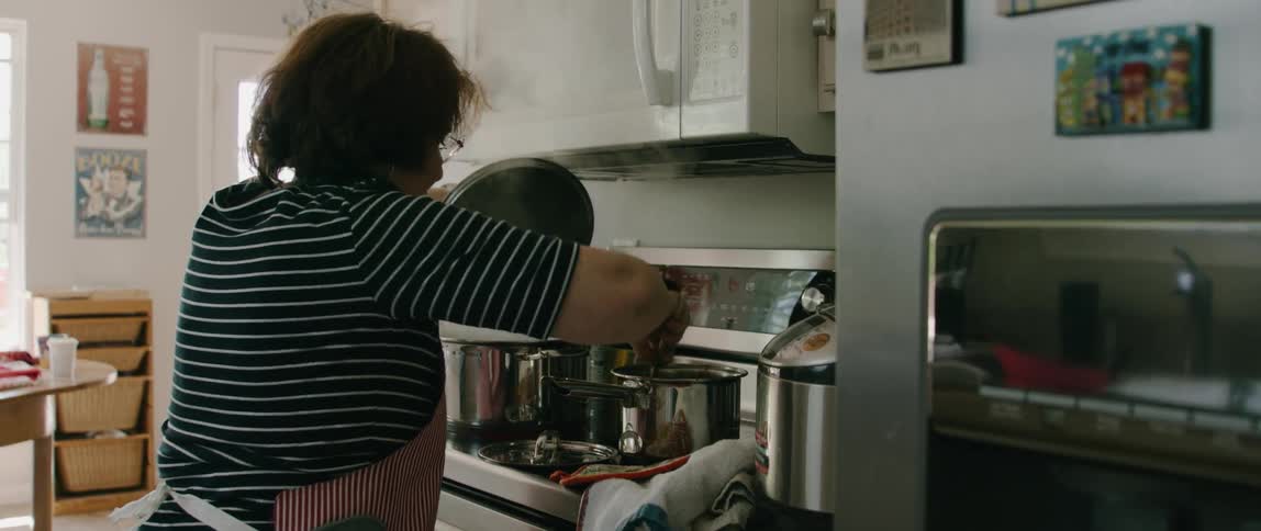 A woman in a kitchen stirring a pot on a stove with a wooden spoon