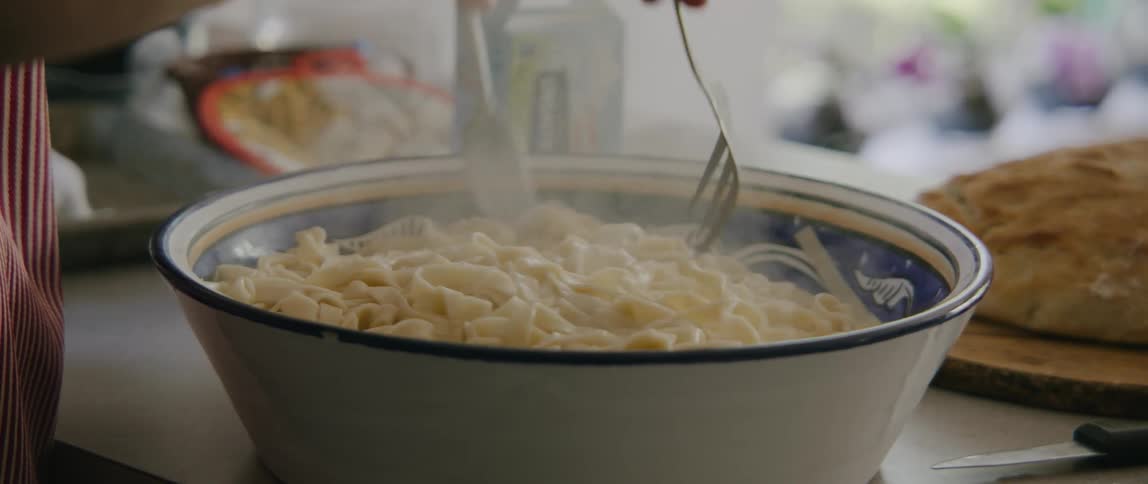 A man laughs as he combines steaming hot pasta and sauce in a bowl