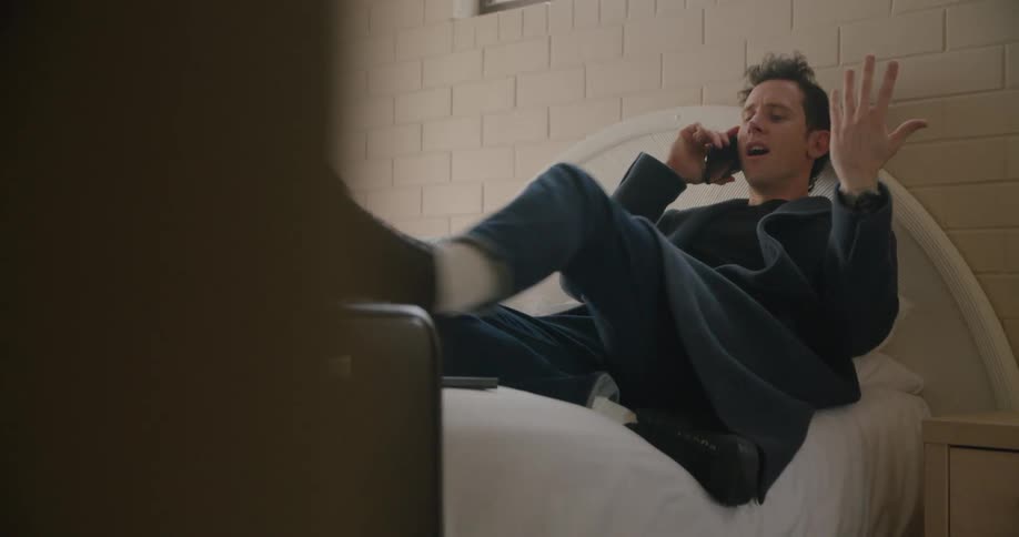 Man reclining on bed and talking on mobile phone puts leg onto bed