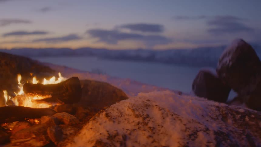 A campfire burns on the side of a snow covered mountain
