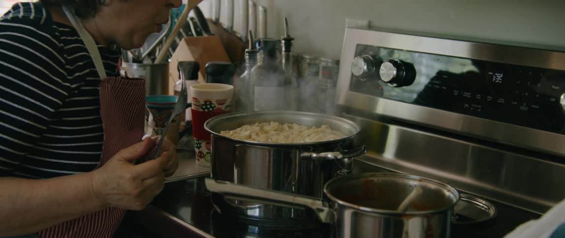 A woman stirring a steaming pot of pasta cooking on a stovetop at home