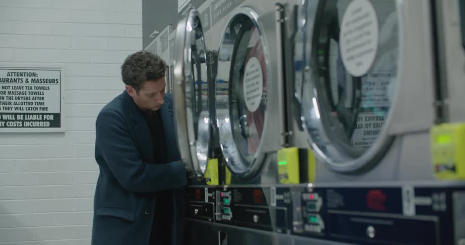 A man in a laundry mat takes his clothes out of a dryer