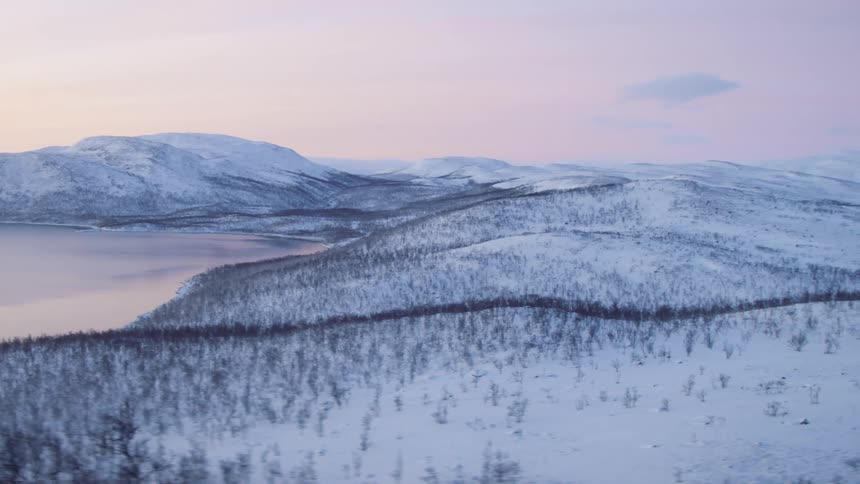 Small trees on the snow covered hills near the mountains at sunset