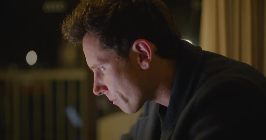 A man takes a drink from a teacup while scrolling through information on his laptop