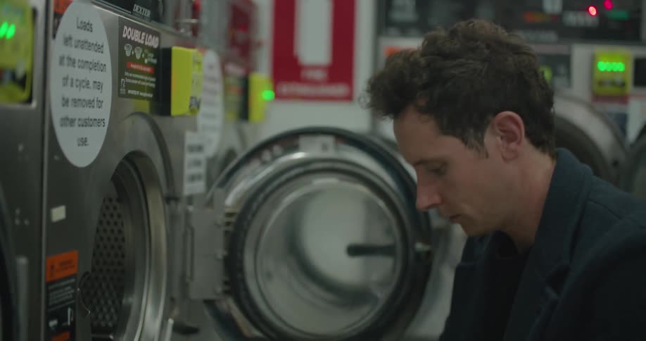 Man loads his laundry into a washing machine at the laundromat