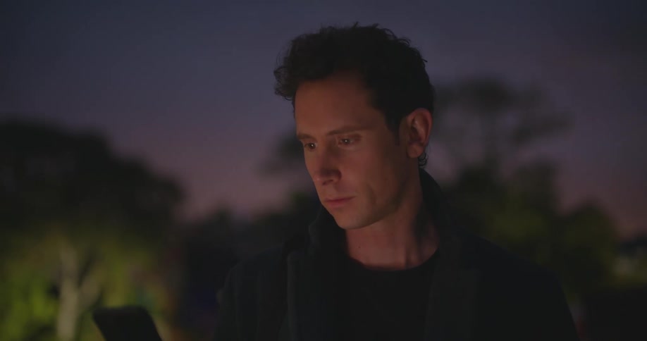 Man with a blazer jacket takes out smartphone to use with purple sky in the background at dusk