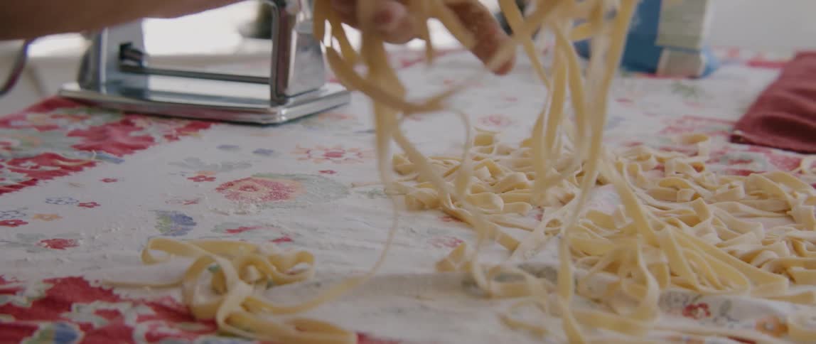 A person in the kitchen making pasta on a table with flour