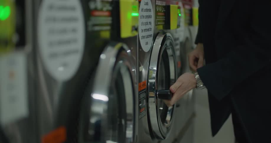 A man adding laundry and detergent to a washing machine in a laundromat