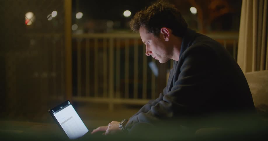 Young man sitting on a couch working on a laptop at night