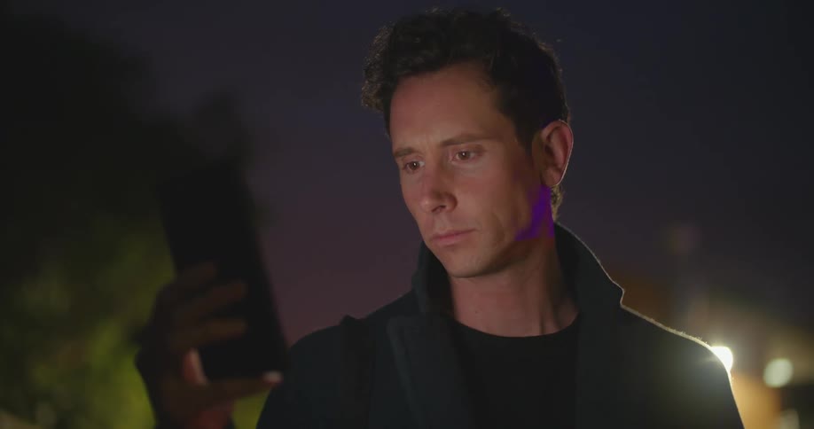 A man stands outdoors in the darkness while looking at his smart phone