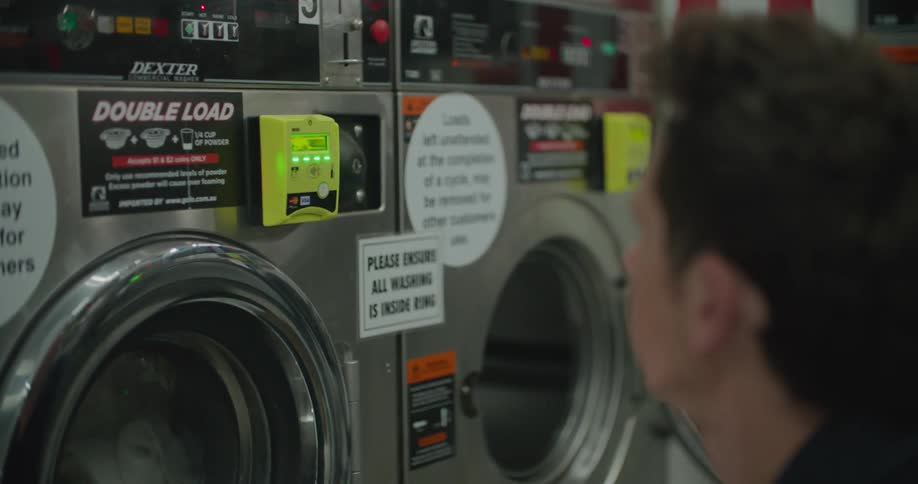 A man with a smart phone putting it up to a washing machine to pay