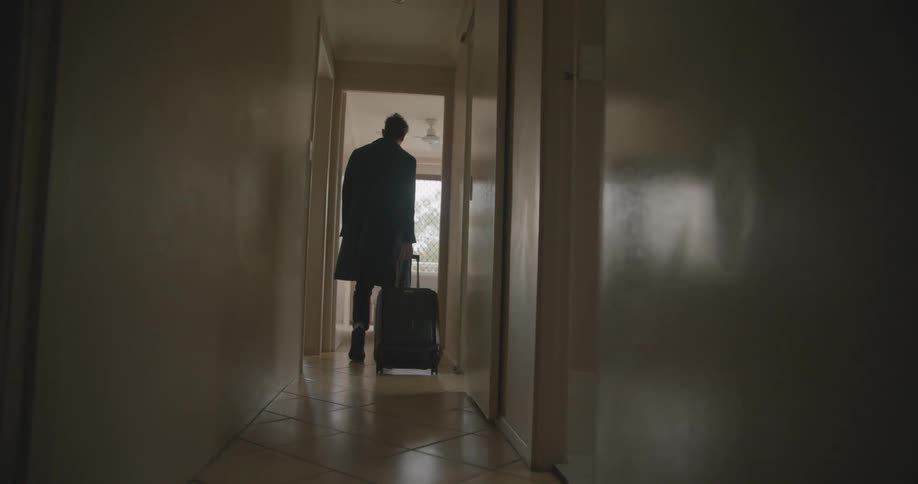 A man pulls his luggage behind him as he walks down a narrow corridor