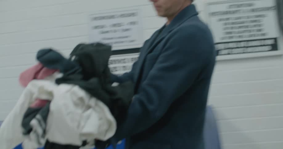 Man removes clothing from a dryer in a laundromat and sets them on a table