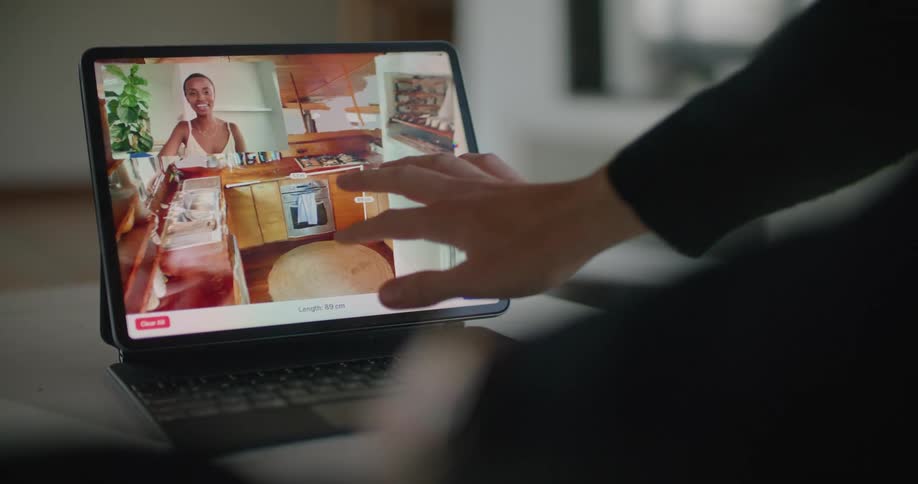 A woman in an office video chats with another woman on a tablet as they look at a kitchen in a home