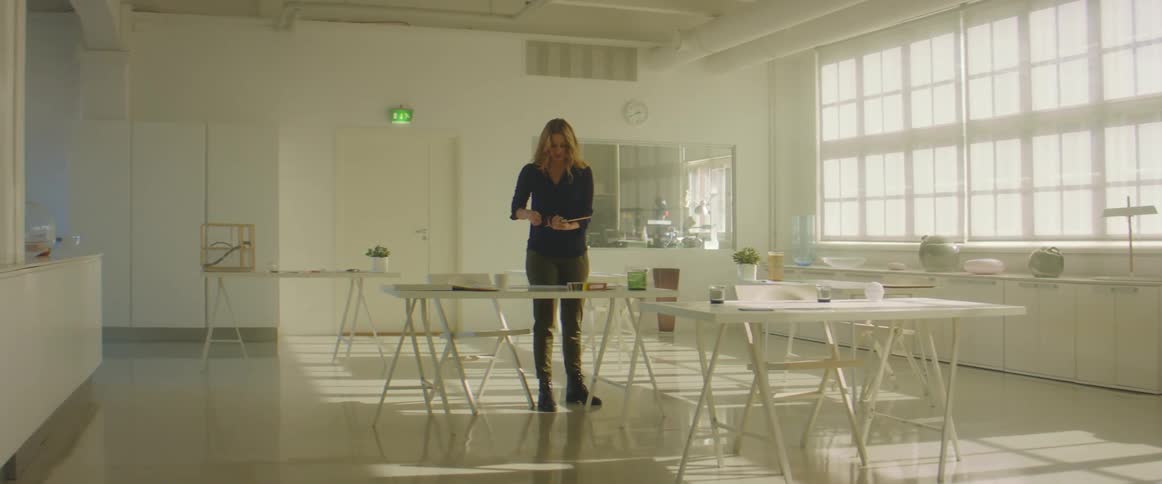 A woman with a mug and a tablet walking into a room with chairs and tables