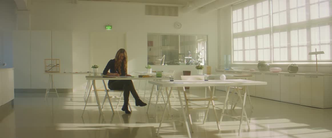 A woman sits at a table in a large room with other tables