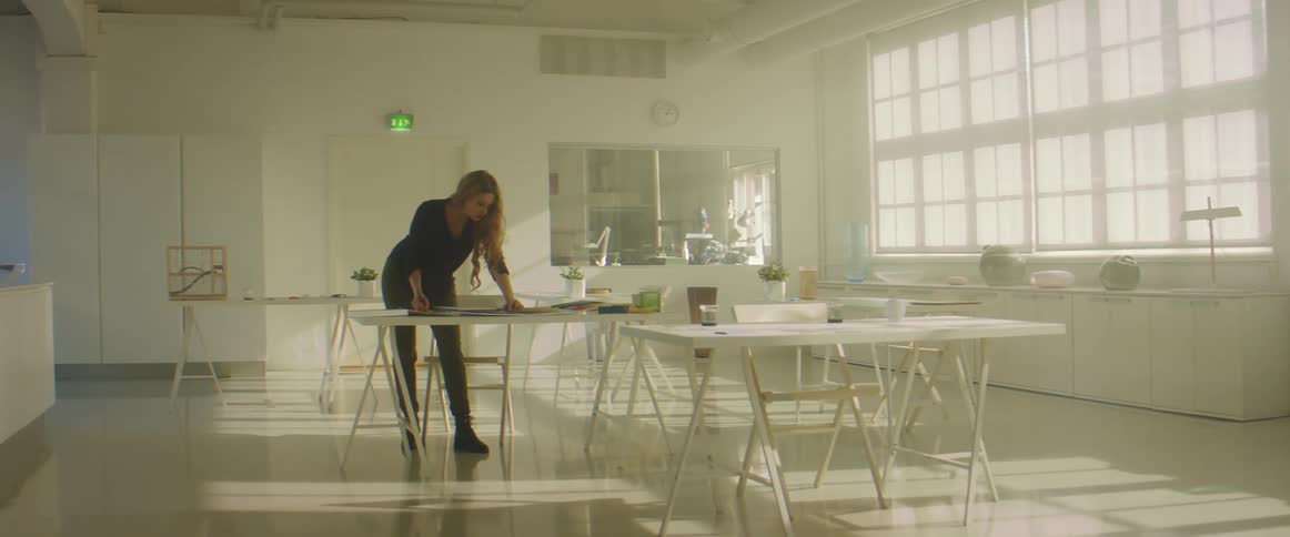 A woman leans over a table looking at items in a large office room