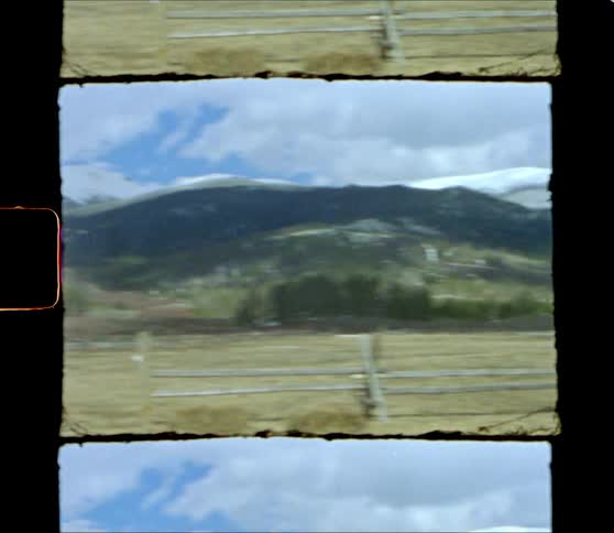 A mountain range in the distance behind a flat open field lined by a wooden fence during the day