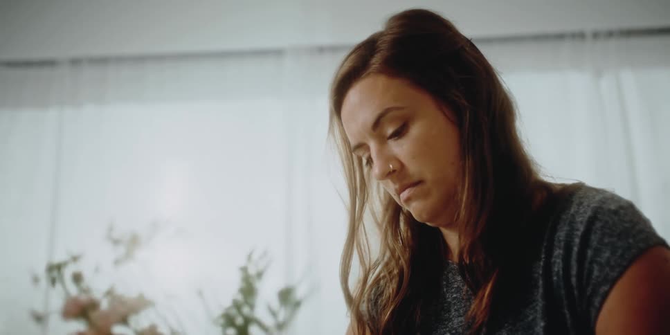 A woman in a room arranging flowers with a wall and window in the background