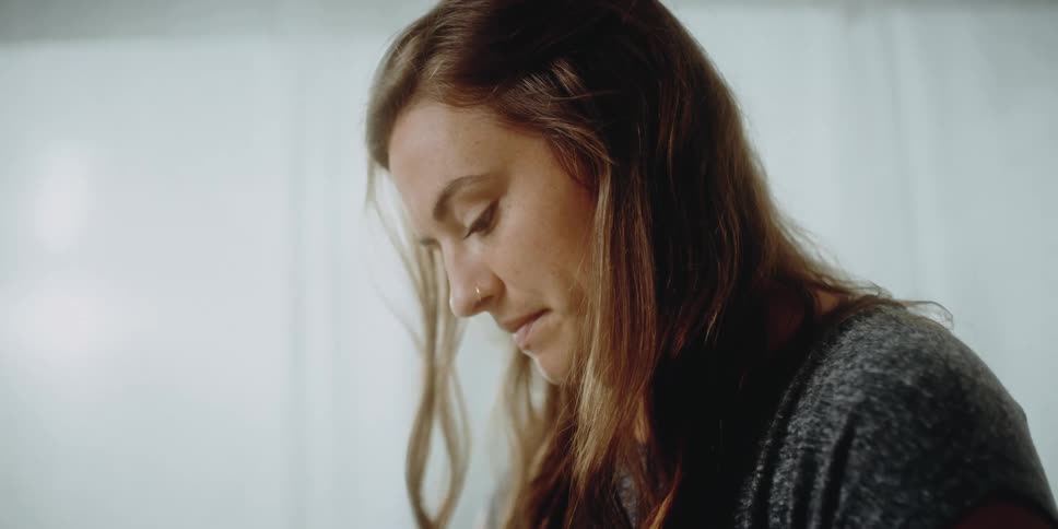 Hair falls around a womans face as she stands while looking down