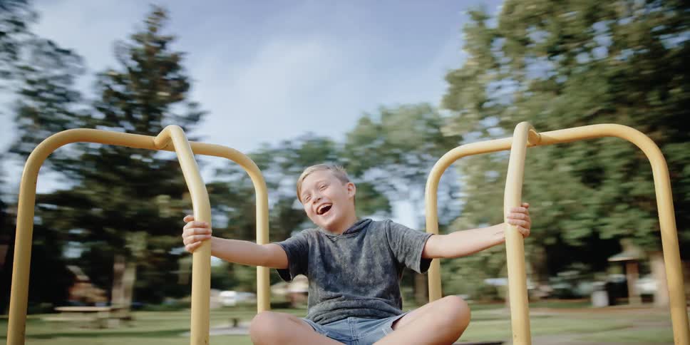 A boy laughs and holds on tight as he spins on a roundabout in the park