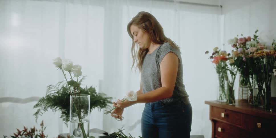 A female florist arranging white roses in a tall glass vase