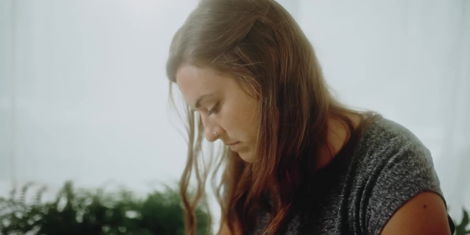 A woman is sitting in a room with her head bowed down