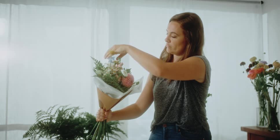 A woman in a room arranging flowers with a wall and window in the background