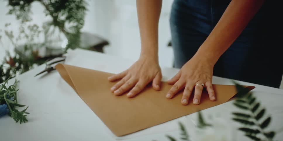 A florist folds brown wrapping paper on a table
