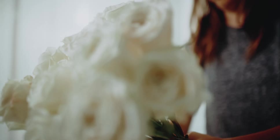 Woman holds a bouquet of white roses and adds more flowers to it