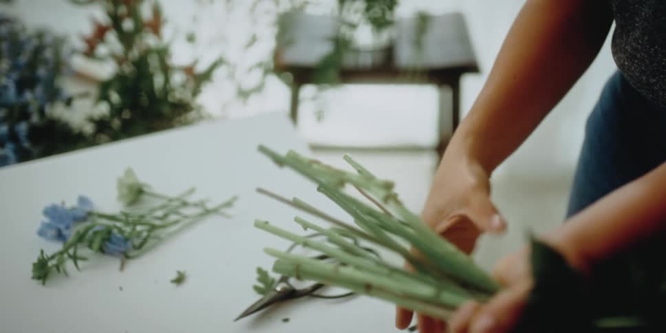 A female florist trims the stems of flowers as she bunches them together