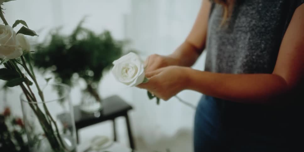 A female florist plucks the petals off of the stem of a white rose
