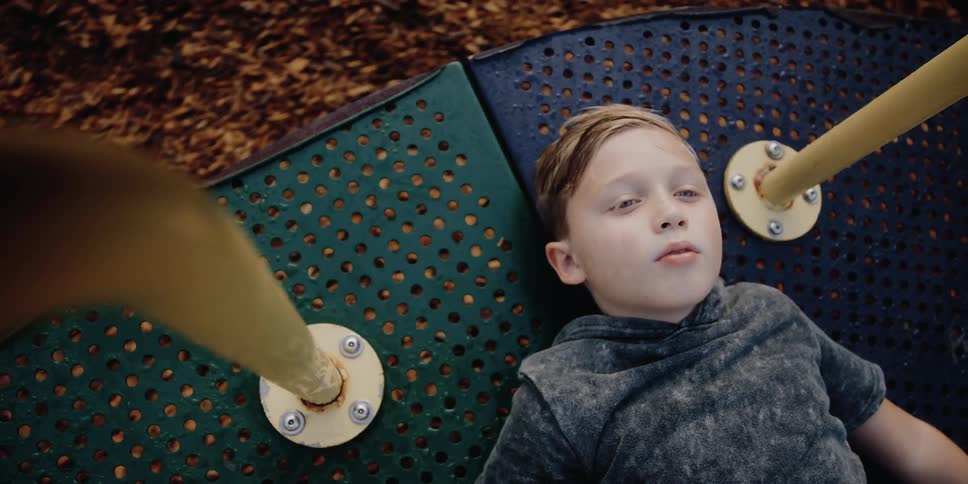 A boy lies on his back on a playground merry go round as it spins