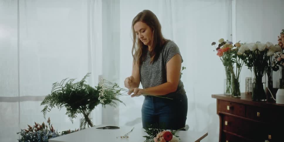 A female florist carefully groups several small flowers together in her hands