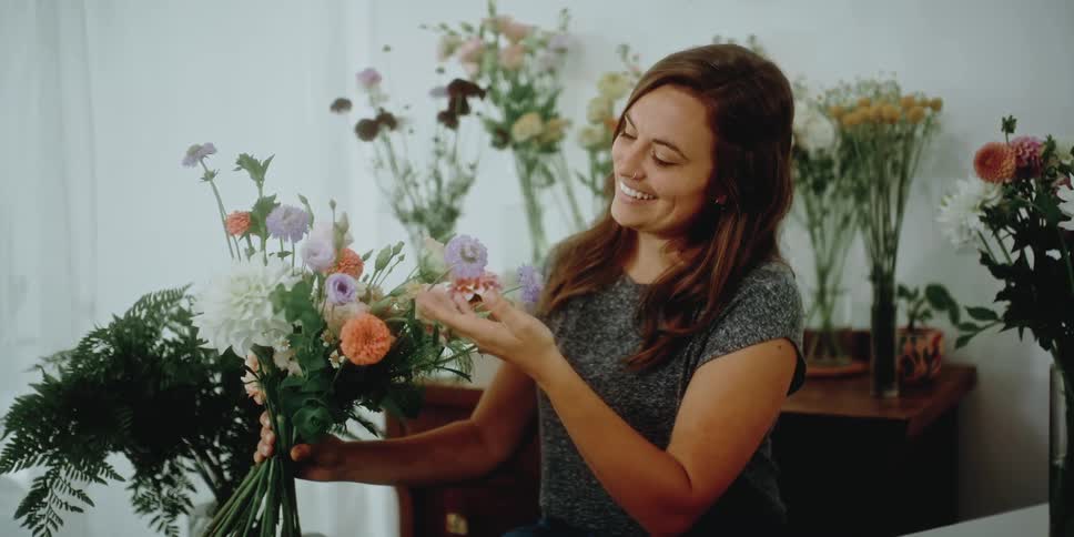 A female florist smiles as she holds a variety of flowers of a floral arrangement