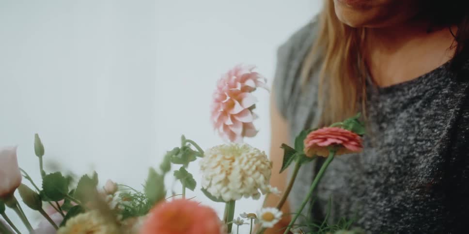 Woman touches and examines flower arrangement before smiling