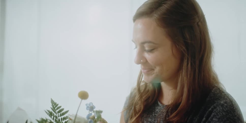 A florist smiles as she picks up a bouquet and smells it