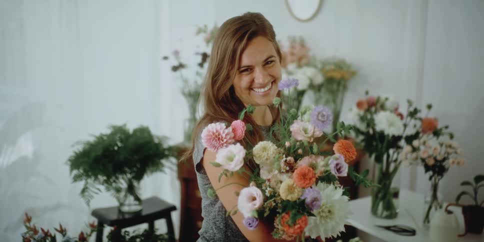 A woman in a room holding a bouquet of flowers with a wall and plants in the background